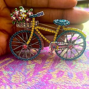 Charming brooch feat. a multi-colored rhinestone bike with a basket w/flowers